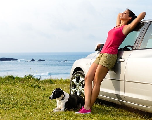 woman-leans-against-car-as-dog-lies-next-to-her Dog lies next to a woman leaning on a car.